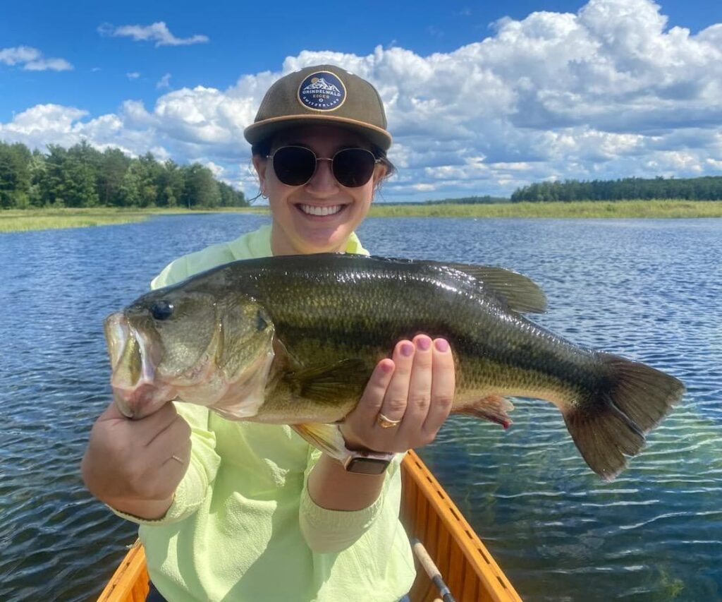 Woman in a canoe holding a freshly caught Largemouth Bass.