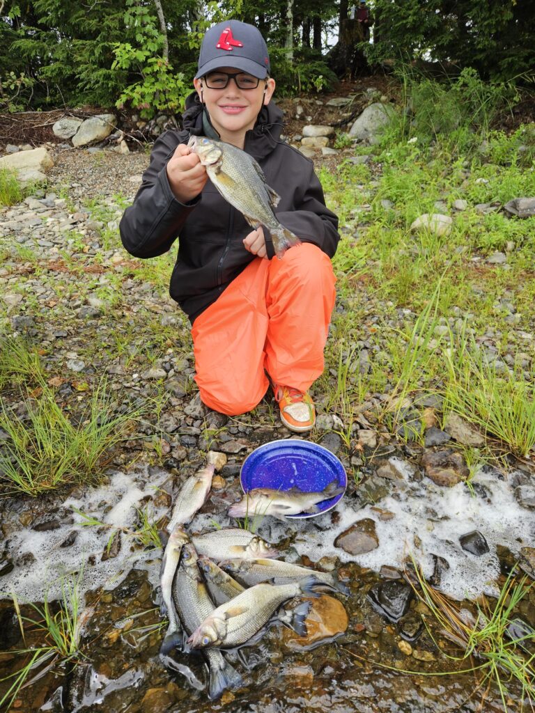 Boy holding a white perch with several more fish on the ground.